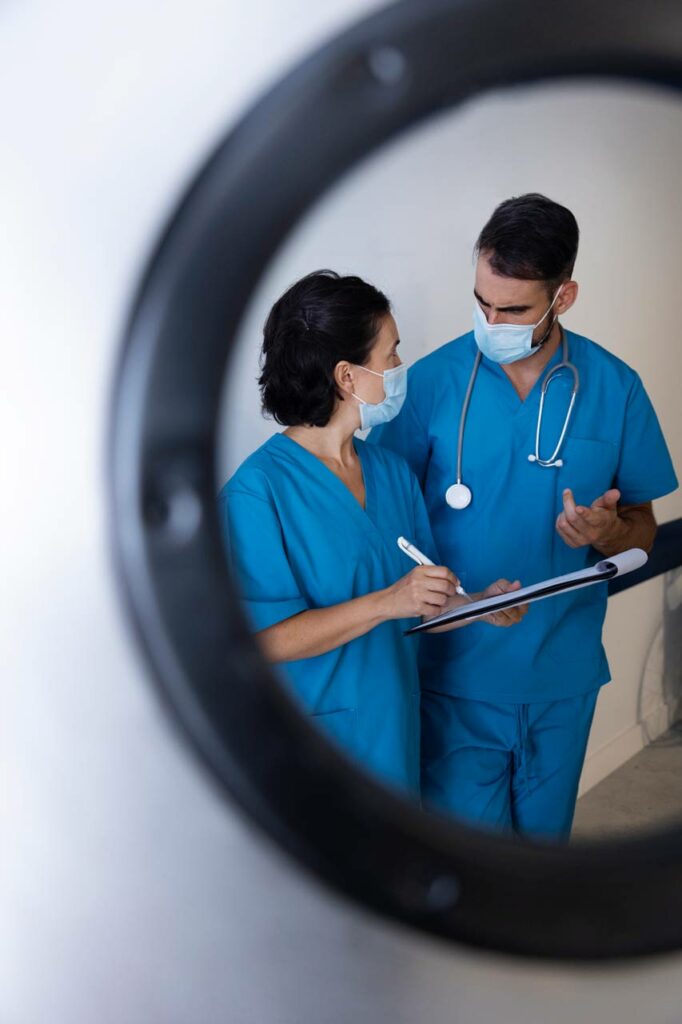 Profesional sanitario con bata verde y estetoscopio cruzado frente a un edificio hospitalario.